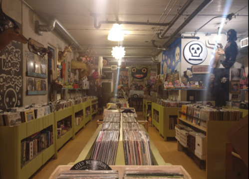 A cozy record store filled with vinyl records, colorful artwork, and eclectic decorations on the walls.