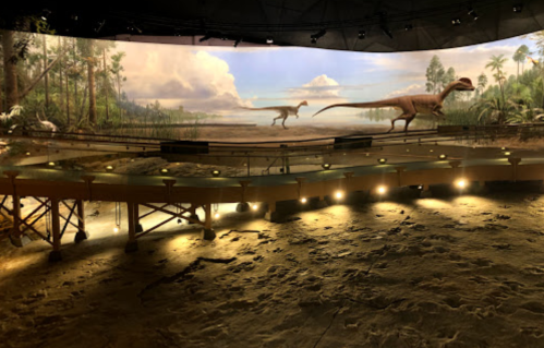A prehistoric scene with two dinosaurs on a stage, surrounded by a lush landscape and dramatic lighting.