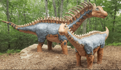 Two large dinosaur sculptures, one adult and one juvenile, surrounded by trees in a natural setting.
