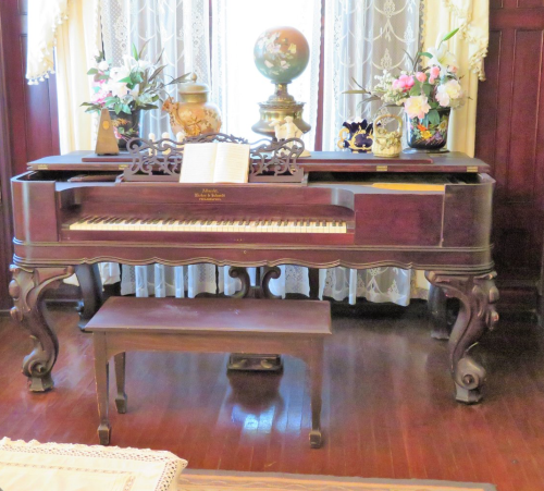 A vintage piano with ornate legs, accompanied by decorative vases and a globe, set in a warmly lit room.