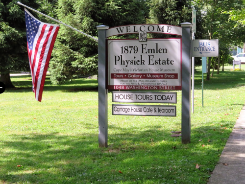 Sign for the 1879 Emlen Physick Estate, featuring tours, a café, and a bus entrance, with an American flag nearby.