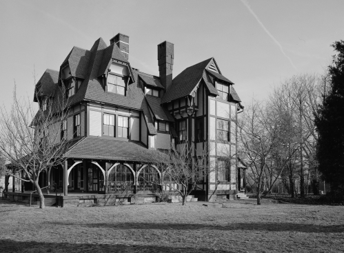 A large, historic house with intricate architecture, surrounded by bare trees and a grassy yard, in black and white.