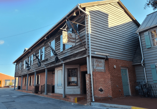 Historic building with wooden siding and brick accents, featuring a sign for "The Pirate House" and a blue door.