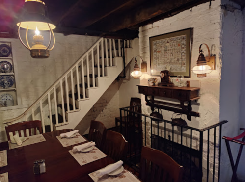 Cozy dining area with wooden tables, chairs, and a staircase, featuring vintage decor and warm lighting.