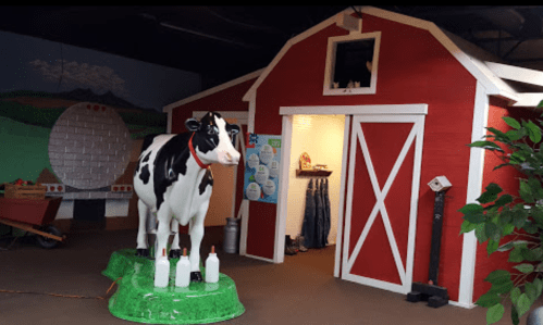 A red barn with a life-sized cow statue and milk bottles, set in a playful farm-themed environment.
