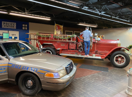 A vintage fire truck inside a police station, with a person inspecting it next to a police car.