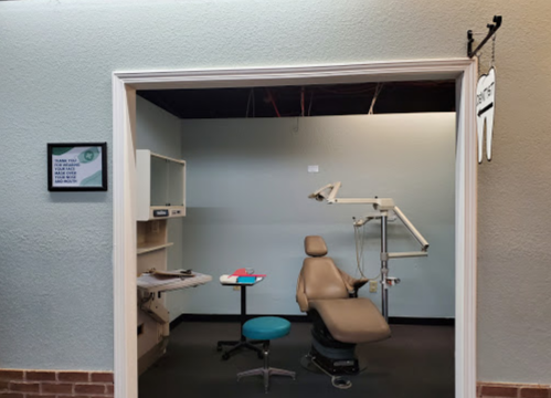 A dental office room featuring a chair, dental equipment, and a small desk with supplies.