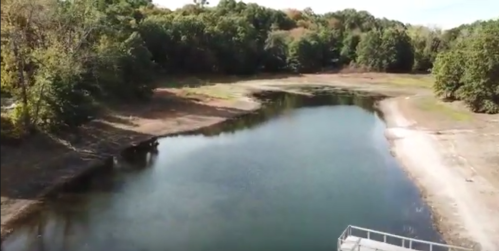 Aerial view of a calm river surrounded by trees, with a dry shoreline and visible sandy areas.