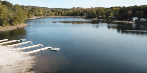 A serene lake surrounded by trees, with wooden docks extending into the water and houses in the background.