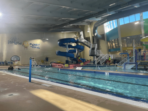 Indoor water park featuring a pool, water slides, and play areas, with sunlight streaming through large windows.