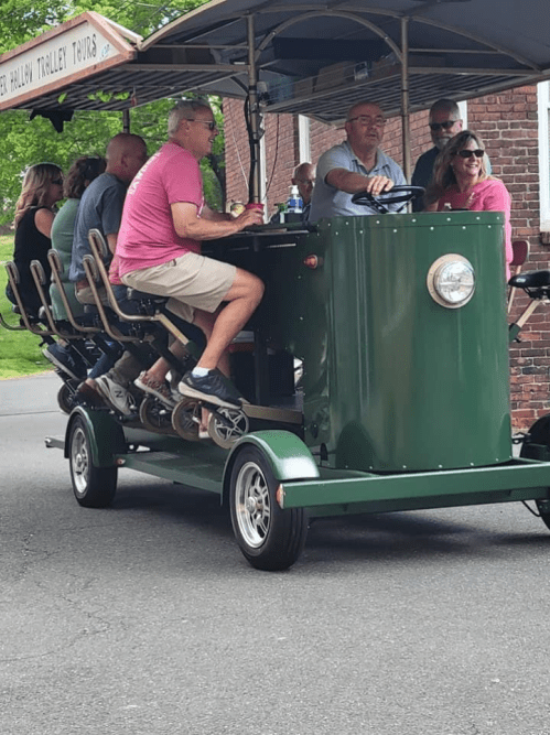 A green trolley with passengers enjoying a tour, featuring a driver at the front and people seated behind.