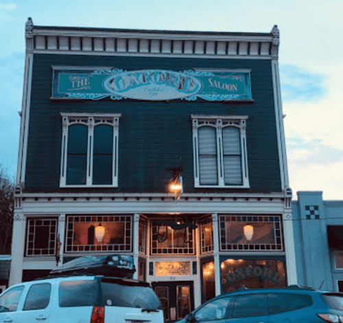 Historic building with a sign reading "The Oxford Saloon," featuring large windows and a vintage facade.