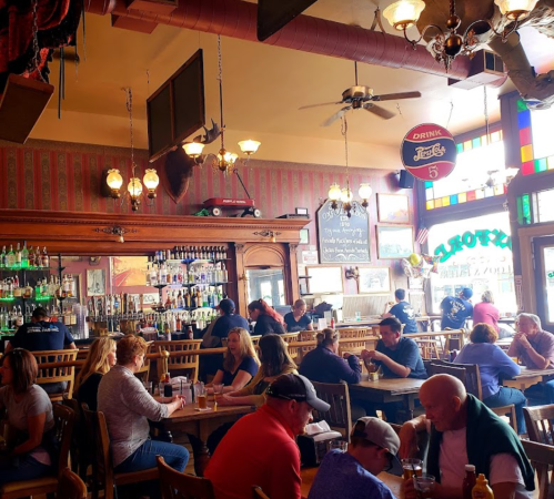 A bustling restaurant interior with patrons dining, a bar with drinks, and colorful stained glass windows.