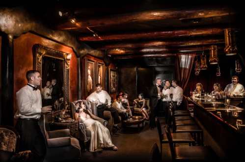 A stylish lounge with elegantly dressed guests socializing, featuring vintage decor and a warm, inviting atmosphere.