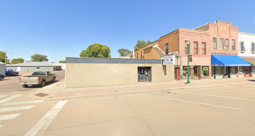 A street view of a small town with a brick building, a blue awning, and a parked truck on a sunny day.