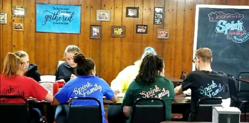 A group of people sitting at a table, wearing matching shirts, enjoying a meal in a cozy, wooden-paneled room.