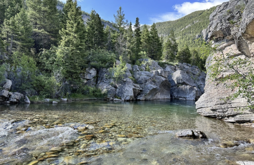 A serene river scene surrounded by lush greenery and rocky cliffs under a clear blue sky.