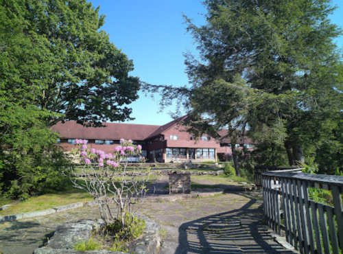 A scenic view of a building surrounded by trees and blooming flowers under a clear blue sky.