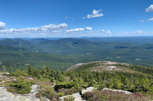A panoramic view of lush green mountains under a clear blue sky with scattered clouds.