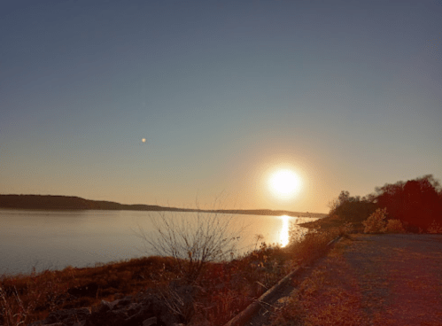 A serene sunset over a calm lake, with silhouettes of trees and a clear sky reflecting warm colors.