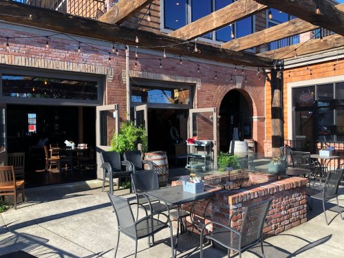 Outdoor dining area with brick walls, wooden beams, and tables set up under string lights.