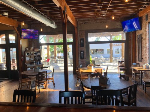 Interior of a rustic restaurant with wooden tables, chairs, and large windows letting in natural light.