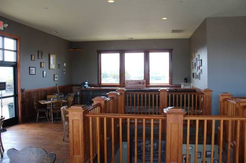 Interior of a cozy restaurant with wooden railings, tables, and large windows letting in natural light.
