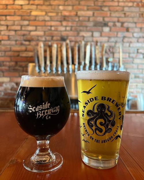 Two glasses of beer on a wooden table: a dark stout in a curved glass and a light lager in a branded pint glass.