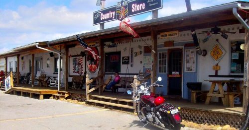 A rustic country store with a motorcycle parked outside, featuring wooden steps and a welcoming atmosphere.