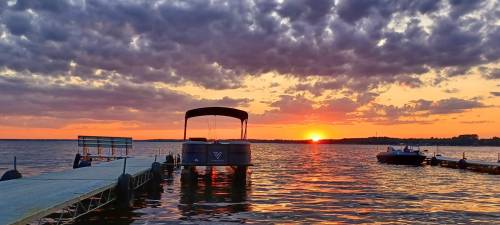 A serene sunset over a lake, with a dock and boats silhouetted against colorful clouds.