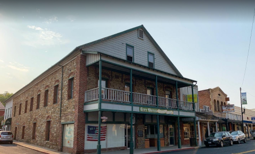 Historic building with a stone facade, balconies, and an American flag, located on a quaint street.