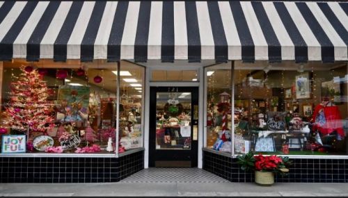 A charming storefront with a striped awning, festive decorations, and a Christmas tree in the window.