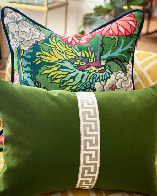 Two decorative pillows on a couch: one with a colorful dragon design and the other in green with a geometric band.