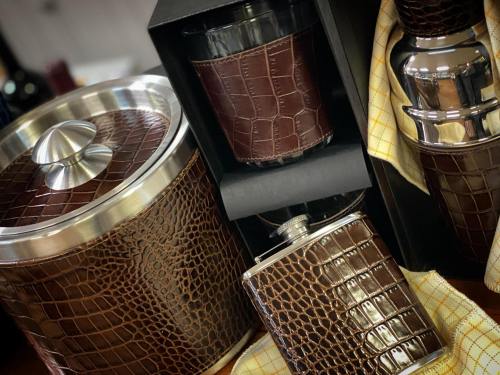 A collection of stylish barware featuring brown crocodile-patterned leather, including an ice bucket, flask, and glass.
