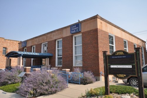 Exterior of Great Western Bank building with a blue awning and purple flowers in front. Signage visible.