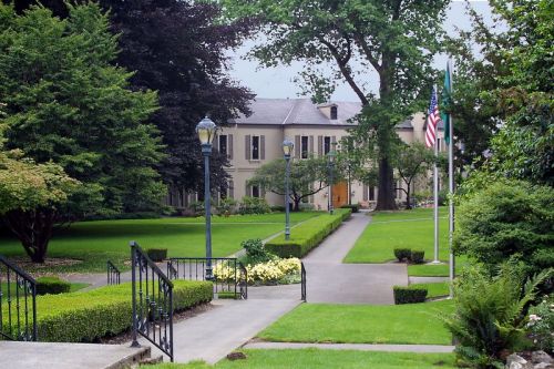 A well-maintained garden with pathways leading to a large, elegant building and American flags in the background.
