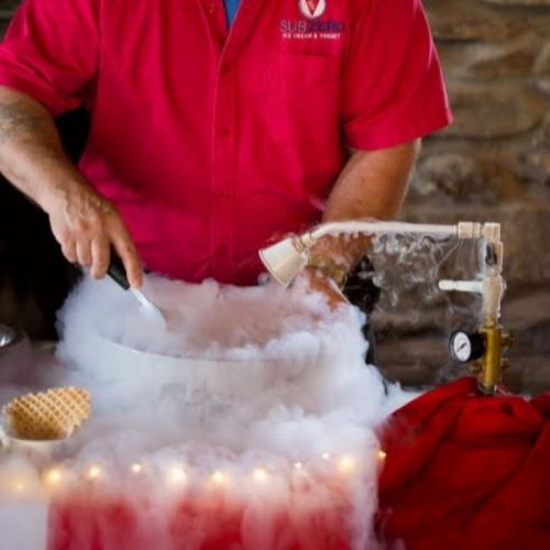 A person in a red shirt prepares a dessert with smoke and a waffle cone on a table.