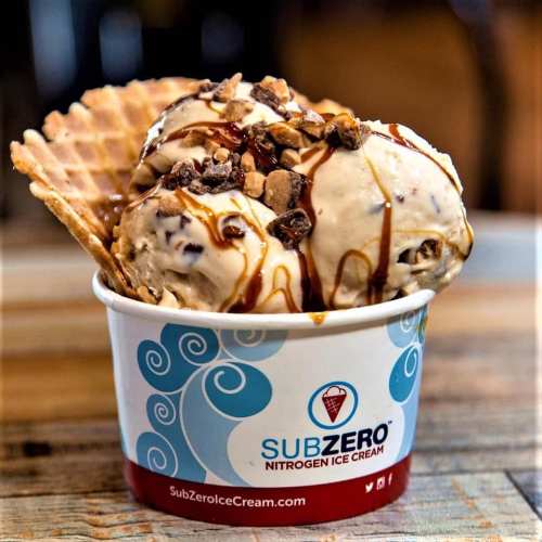 A cup of nitrogen ice cream topped with caramel drizzle, nuts, and chocolate pieces, served in a waffle cone.