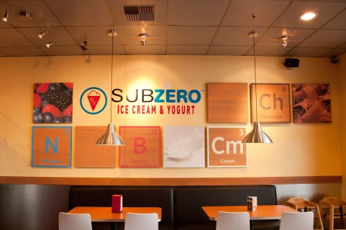 Interior of an ice cream shop featuring the "Sub Zero" logo and colorful wall art with letters and flavors.