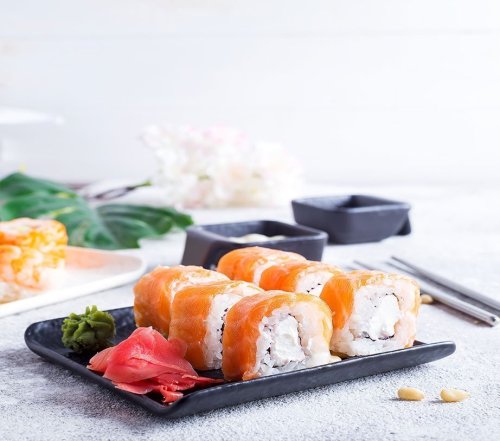 A plate of sushi rolls topped with salmon, accompanied by pickled ginger and wasabi, set on a light background.