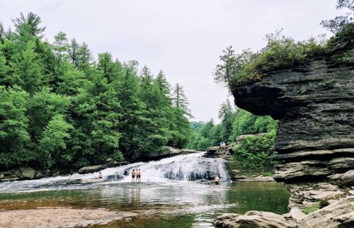 A serene waterfall surrounded by lush greenery, with people enjoying the water and rocky formations nearby.