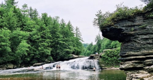 A serene waterfall surrounded by lush greenery, with people enjoying the water and rocky formations nearby.