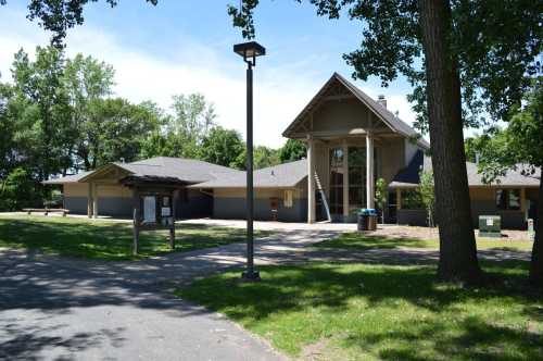 A modern building surrounded by trees and grass, with a pathway leading to the entrance. Clear blue sky above.