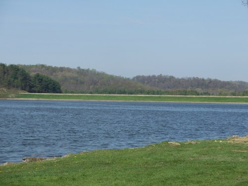 A serene lake surrounded by green hills and trees under a clear blue sky.