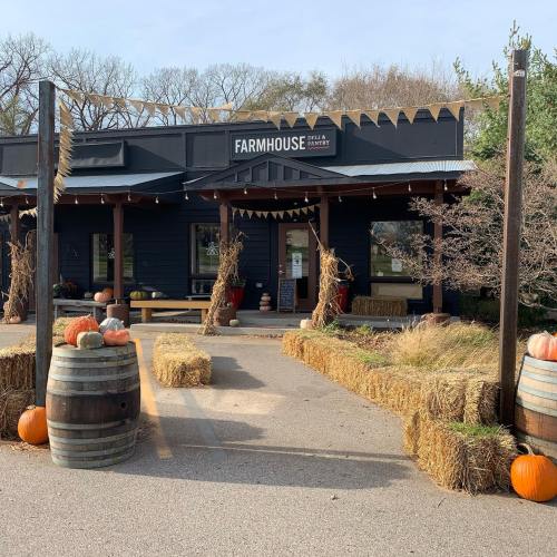 A rustic farmhouse with a black exterior, surrounded by hay bales and pumpkins, set in a rural landscape.