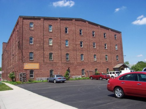 A large red brick building with multiple windows, surrounded by parked cars and a clear blue sky.
