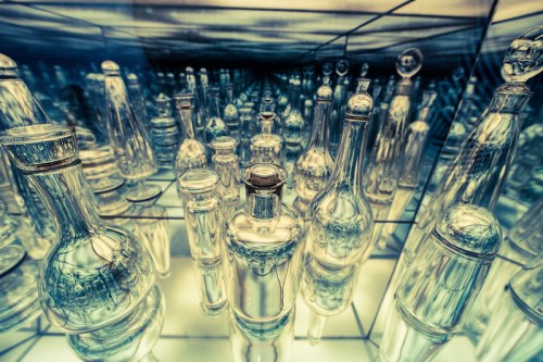 A collection of clear glass bottles reflected in a mirrored space, creating a mesmerizing visual effect.