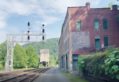 A quiet railway scene featuring an old brick building, signal lights, and lush greenery in the background.