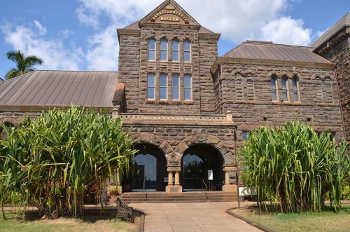 Historic stone building of the Queensland Museum, featuring arched entrances and lush greenery in the foreground.