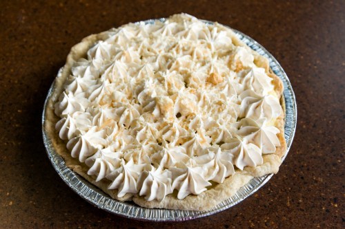 A creamy pie topped with swirls of whipped cream and sprinkled with coconut flakes, in a silver pie tin.